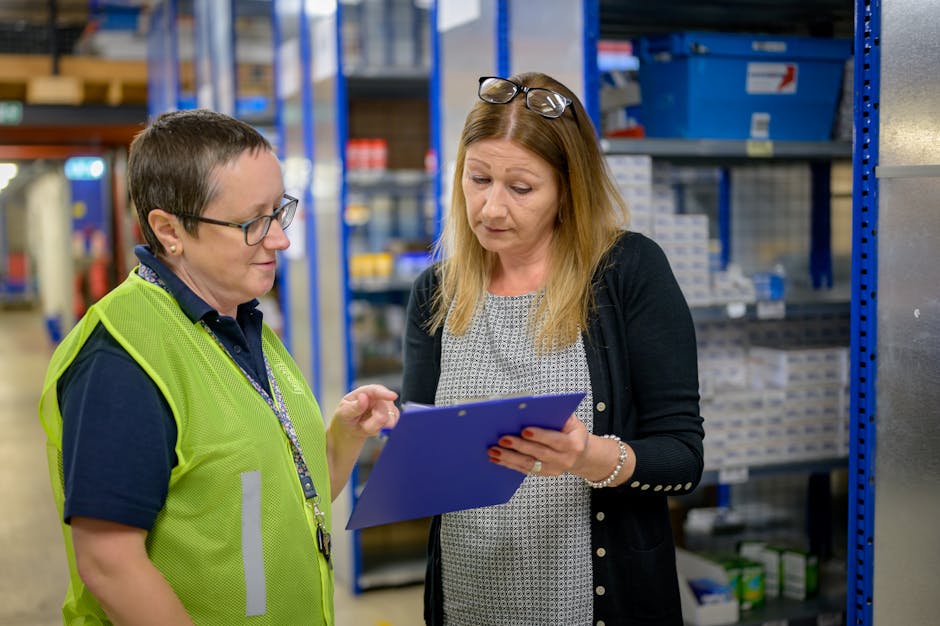 Two women in a warehouse reviewing an inventory checklist on a clipboard.