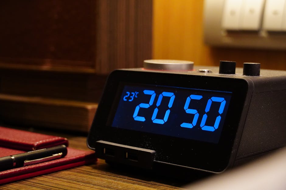 Close-up of a digital alarm clock displaying 20:50 and temperature on a wooden desk with a notepad.